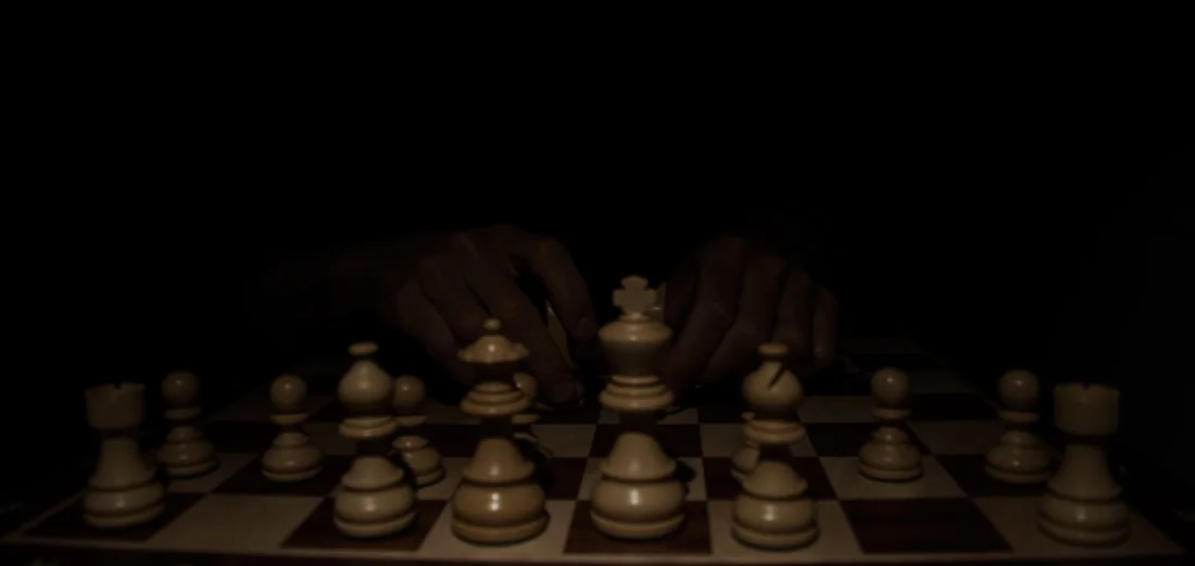 Hands over a chess board in near darkness