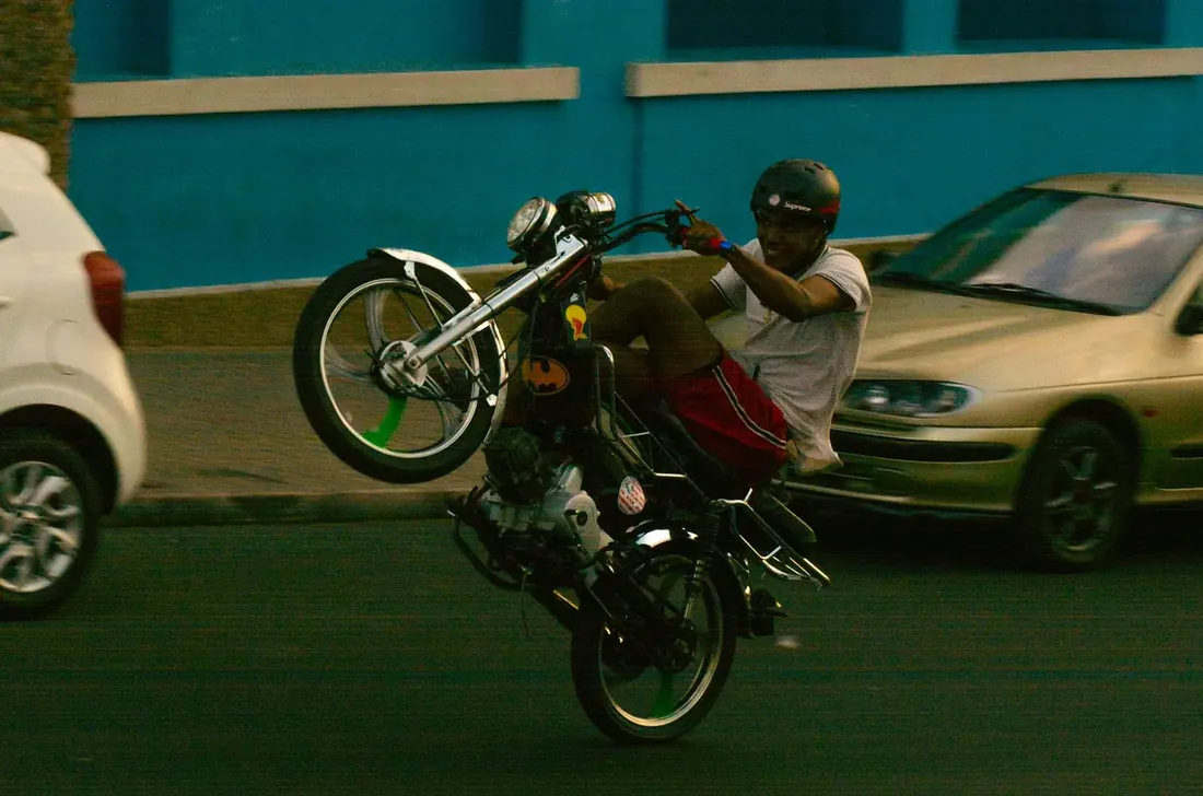Rider on a moped doing a wheelie in front of a blue wall
