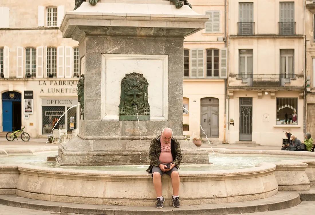Man looking at his phone on the edge of a fountain