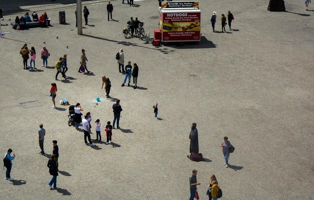 A square seen from above, a hot dog stand and a small child reaching up