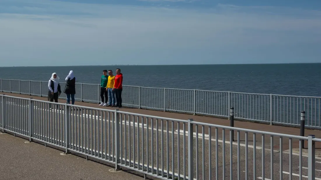 Three men in green, yellow and red and two women in white by a railing at the sea