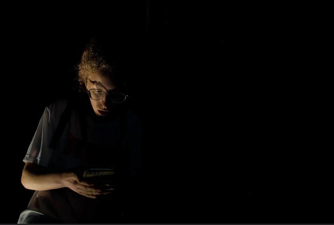 Person in glasses lit by a phone in the dark